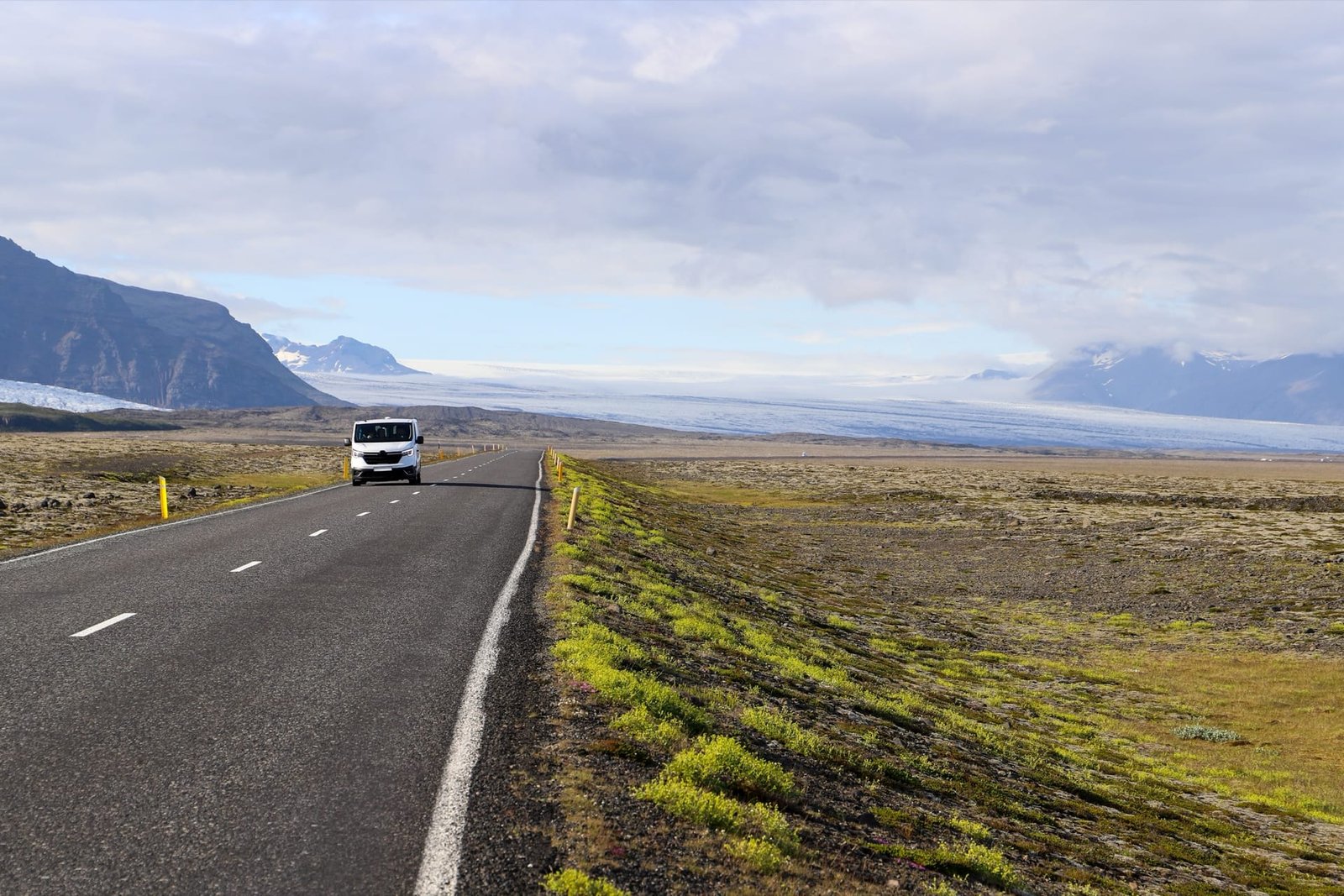 A white van on an empty road across the south of Iceland, a glacier spreading below the mountains ahead