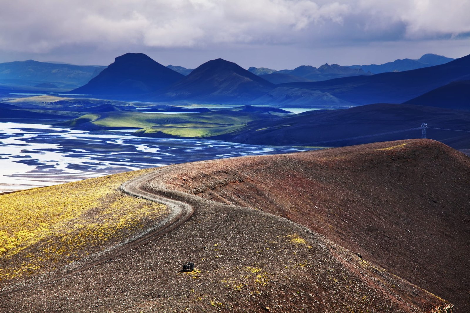 Gravel road winding along a volcanic ridge toward blue highland mountains in Iceland