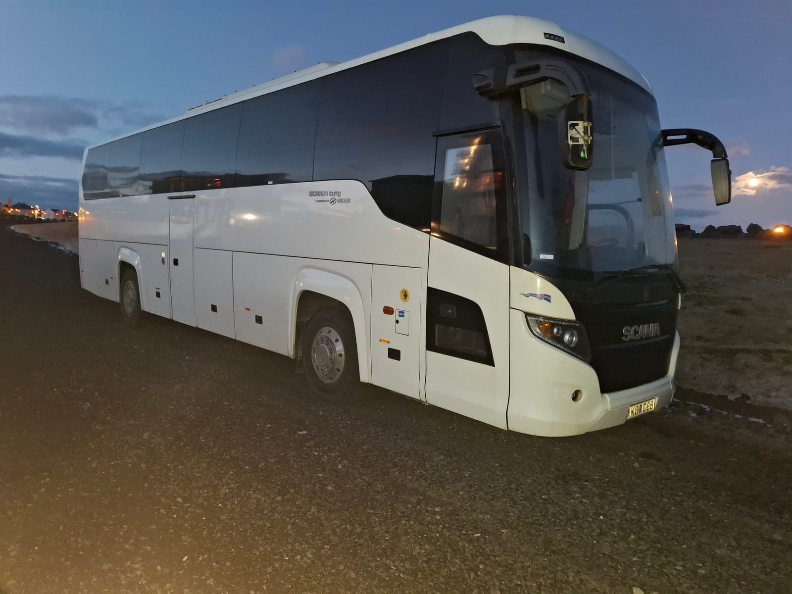 White Scania Touring coach parked on black lava gravel at dusk in Iceland