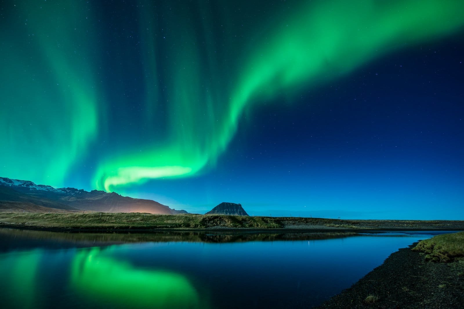 Aurora borealis in green ribbons above Kirkjufell mountain and a still lake, Iceland