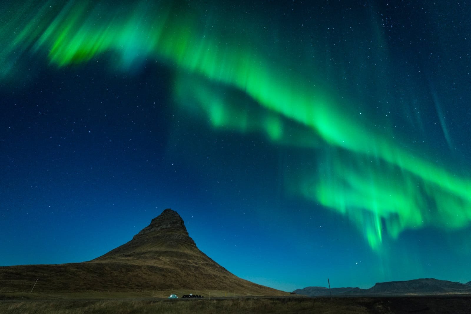 Green aurora curtains above Kirkjufell mountain at night