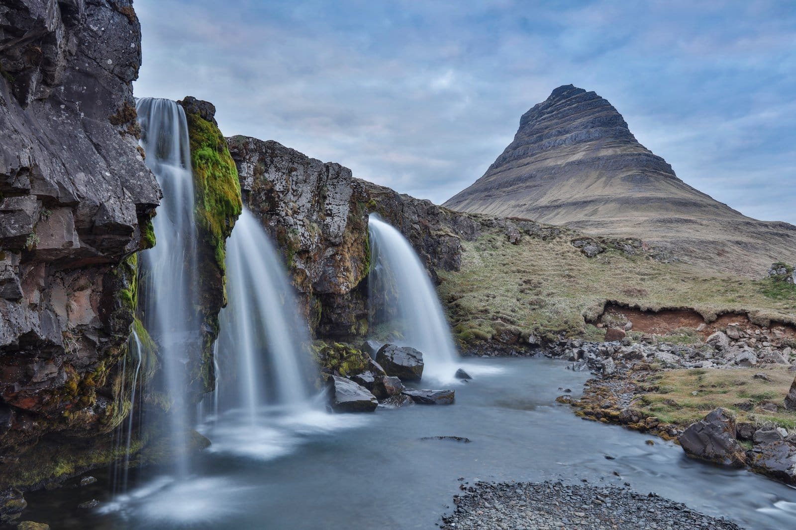 Kirkjufell mountain under a moody sky with its waterfall in the foreground