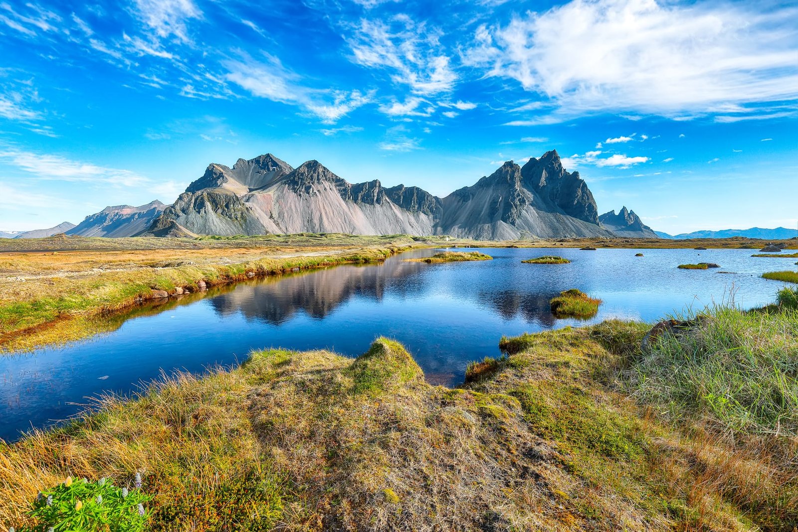 Vestrahorn mountains mirrored in calm water on a sunny day at Stokksnes cape, Iceland